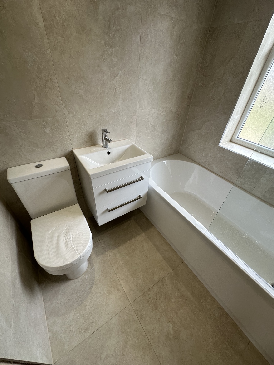 Completed beige tiled bathroom with bath, toilet and wall-hung vanity unit