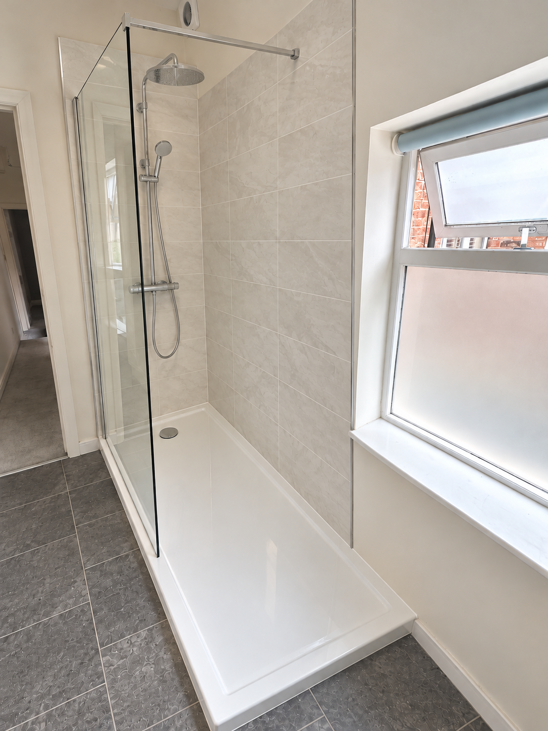 Walk-in shower design with light stone-effect tiles and chrome rainfall shower